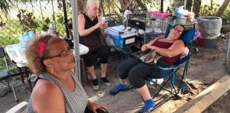 Three women sitting on chairs on a sidewalk.