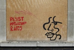 Boarded window with "Resist Immigration Raids" sprayed on it, referring to ICE raids.