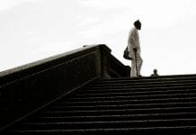 Man with a cane stands at the top of set of stairs in a park .