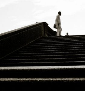 Man with a cane stands at the top of set of stairs in a park .