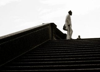 Man with a cane stands at the top of set of stairs in a park .