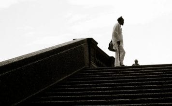 Man with a cane stands at the top of set of stairs in a park .