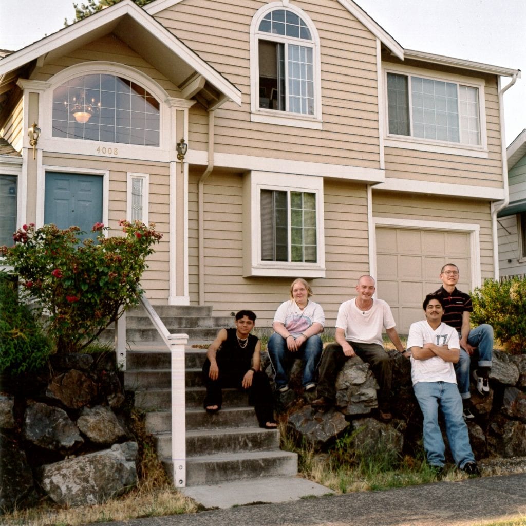 A group of people stand outside a home used for transitional housing after it lost funds due to the City of Seattle diverting resources to rapid re-housing.