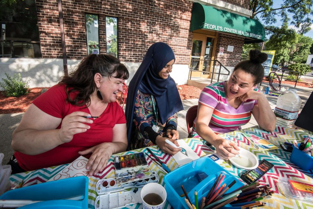 Three Minneapolis residents chat while sitting at a table outdoors.