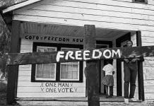 A historical photo of a burned cross with the word "Freedom" in white across it.