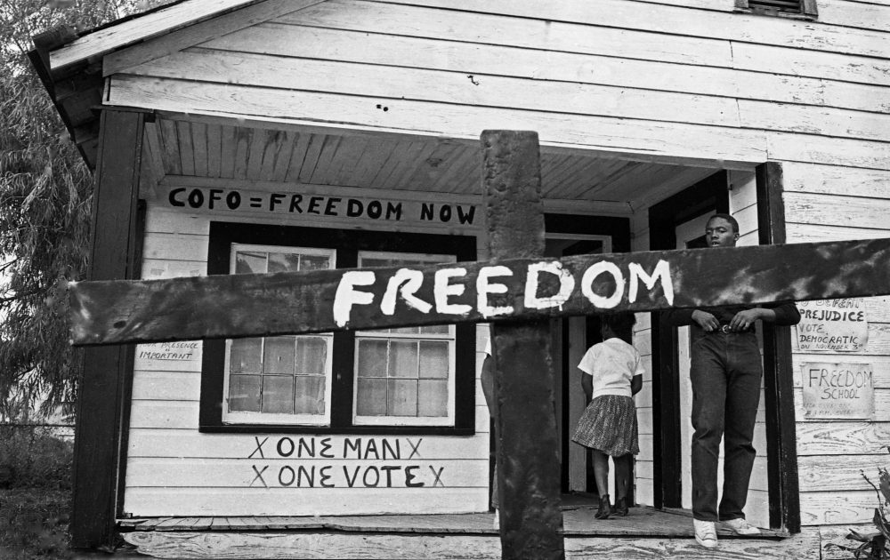 A historical photo of a burned cross with the word "Freedom" in white across it.