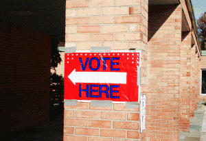 "vote here" sign posted on a brick wall