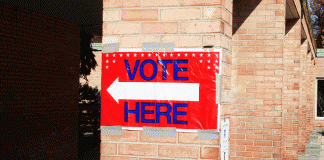 "vote here" sign posted on a brick wall