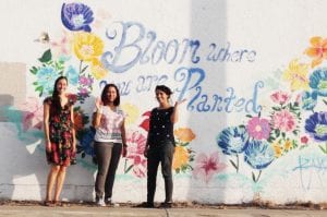 Three women stand in front of outdoor mural.