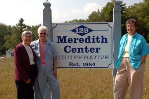 3 women posed at the sides of a sign.