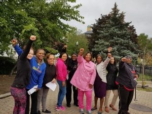 Nine African-American women stand in a park with their fists raised.