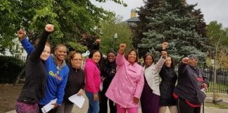 Nine African-American women stand in a park with their fists raised.