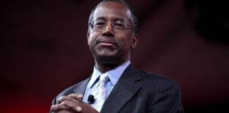 HUD Secretary Ben Carson smiles as his folds his hands in front of his chest.