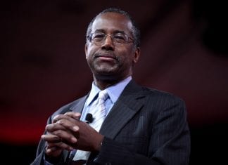 HUD Secretary Ben Carson smiles as his folds his hands in front of his chest.