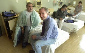 Dr. Jim O’Connell sits on a patient's bed at Pine Street Inn Supportive Housing in Boston.
