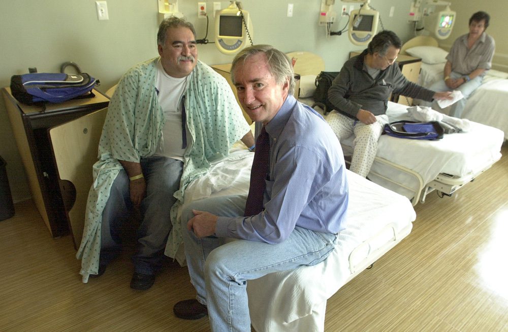 Dr. Jim O’Connell sits on a patient's bed at Pine Street Inn Supportive Housing in Boston.