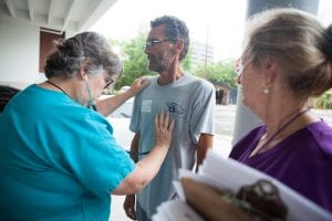 A woman checks a homeless man's heart rate.