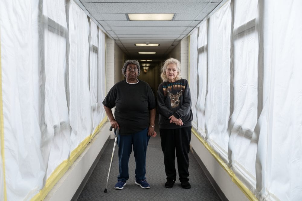 Two older women stand side-by-side in a corridor in a building in Pittsburgh.