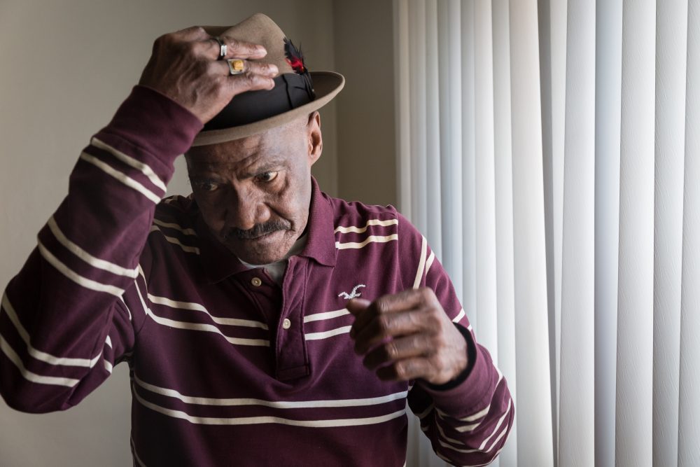 An older African-American man puts on his hat in his Pittsburgh apartment.