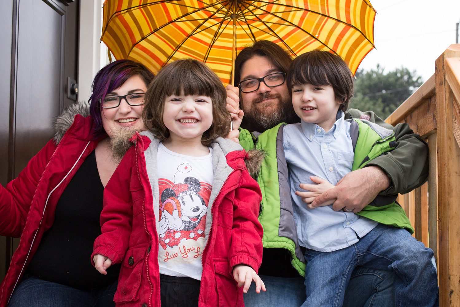 A family of four sit under an umbrella in front of the land trust home.