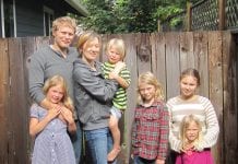 A husband and wife stand in front of a fence along with their five children.