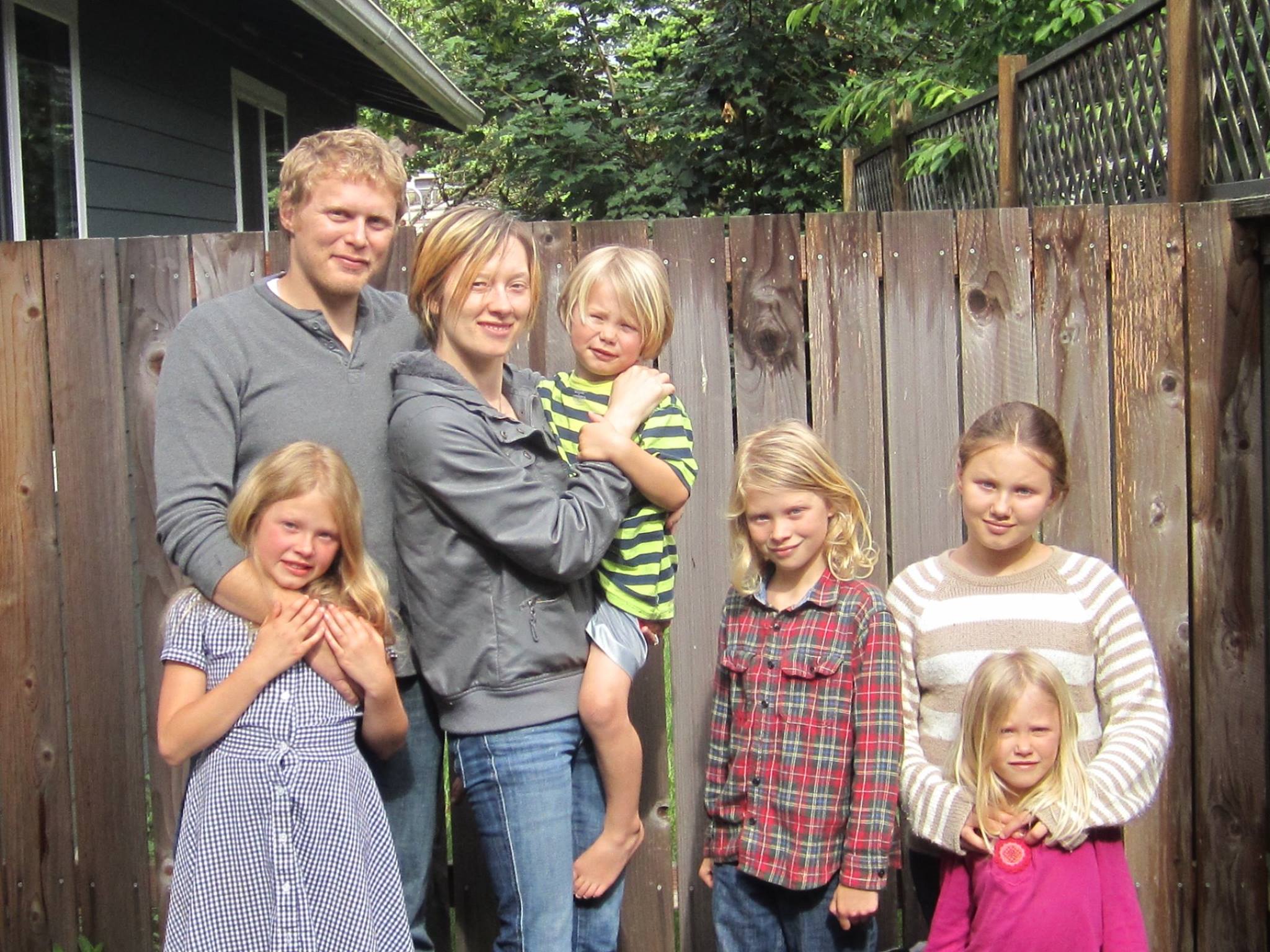 A husband and wife stand in front of a fence along with their five children.