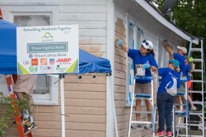 Five people wearing blue shirts paint the side of a home.