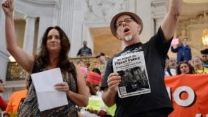 Carin McKay and Chris Carlsson at City Hall during a Mission No Eviction protest in 2015. Charlsson holds a sign that reads "We support the Pigeon Palace becomming a SF Community Land Trust."