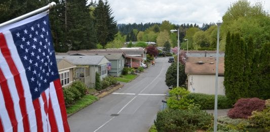 A view of a community in Oregon, with an American flag framing the left hand side. Lots of trees in the area.