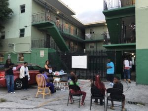 A group of people gather outside an apartment complex to discuss community land trusts.