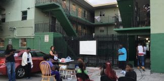 A group of people gather outside an apartment complex to discuss community land trusts.