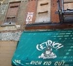 A vacant building in New York City that has boarded up windows and a "Get Rich" signs for a kid cut.