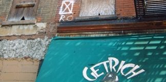 A vacant building in New York City that has boarded up windows and a "Get Rich" signs for a kid cut.