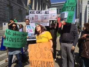 Laura Foote (in yellow shirt at center) at a counter-protest to a rally opposing statewide upzoning bill SB 827. She's surrounded by fellow protestors who are holding signs that read "We Need More HOmes" and "More Homes for All."