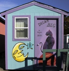 A tiny house has an inspirational saying painted on its door.