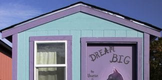 A tiny house has an inspirational saying painted on its door.