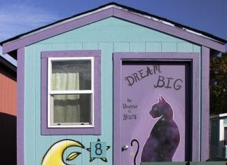 A tiny house has an inspirational saying painted on its door.