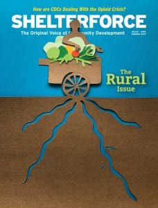 The cover of the summer 2019 edition of Shelterforce magazine, which provides rural coverage, is a cutout of a person behind a wage that contains fruit. 