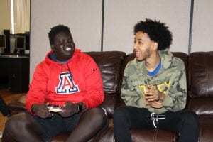 Two young men sit on a sofa playing video games as part of The Hub in San Diego, a healing space for young men of East African descent.