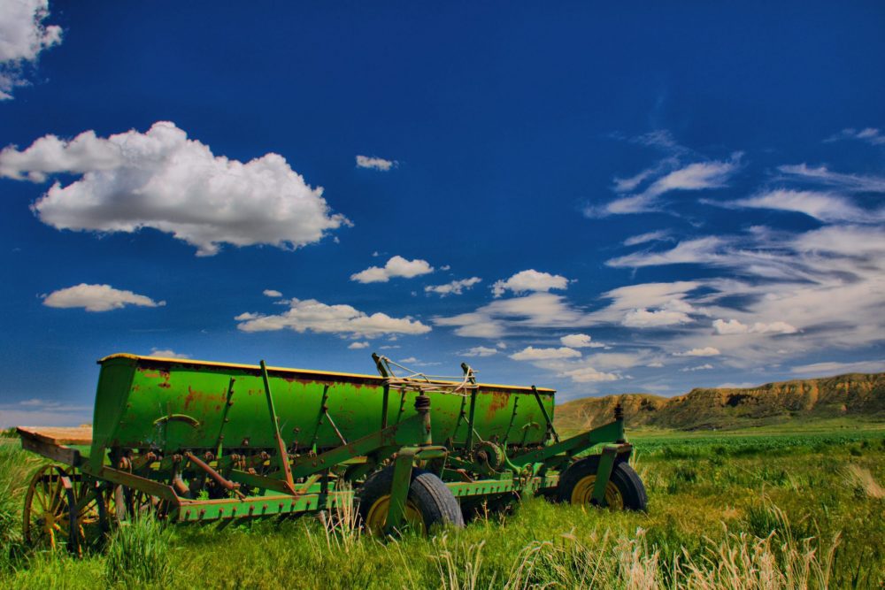 Farm equipment on grass in Montana, with a blue sky with puffy white clouds.