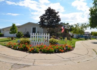 A small white fense with a sign that reads "welcome" and red flowers frame a resident-owned community in Wisconsin.
