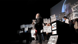 As part of a CultureBank Dallas program, people are on theatre stage with signs as part of a performance.