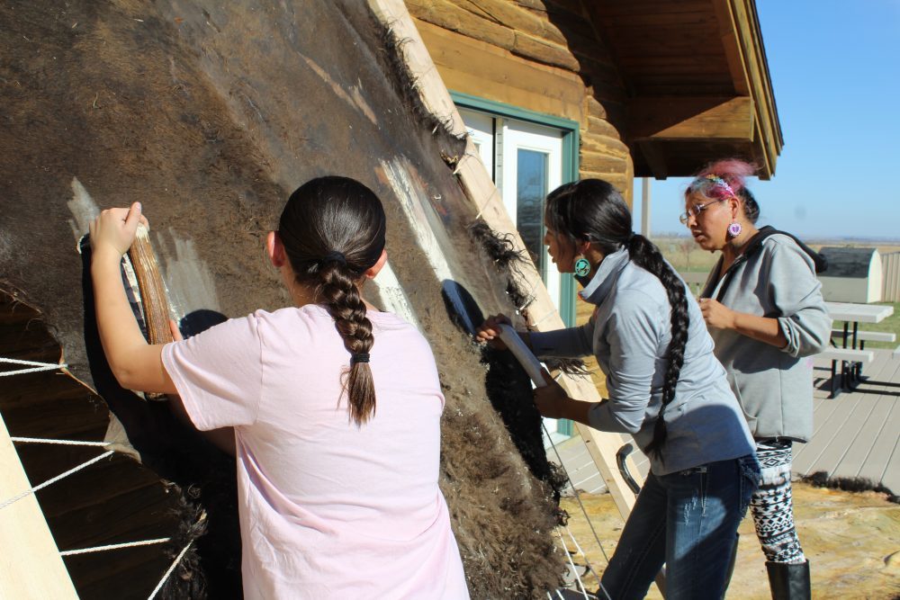 Native women tan hide outside as part of a program called Indigenous Visionaries