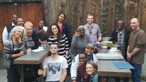 A group of people that are part of the Homecoming Project gather around two tables and smile for a camera.