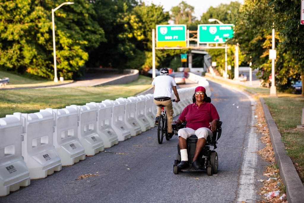 A woman wearing sitting in a motorized wheelchair smiles as she navigates her way up a temporary path in Baltimore.