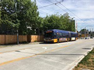 A blue and yellow bus is stopped along a Seattle street that has three lanes, the middle is for turning only.