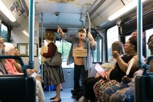 A woman, wearing a sign, stands and points a finger inside a bus.