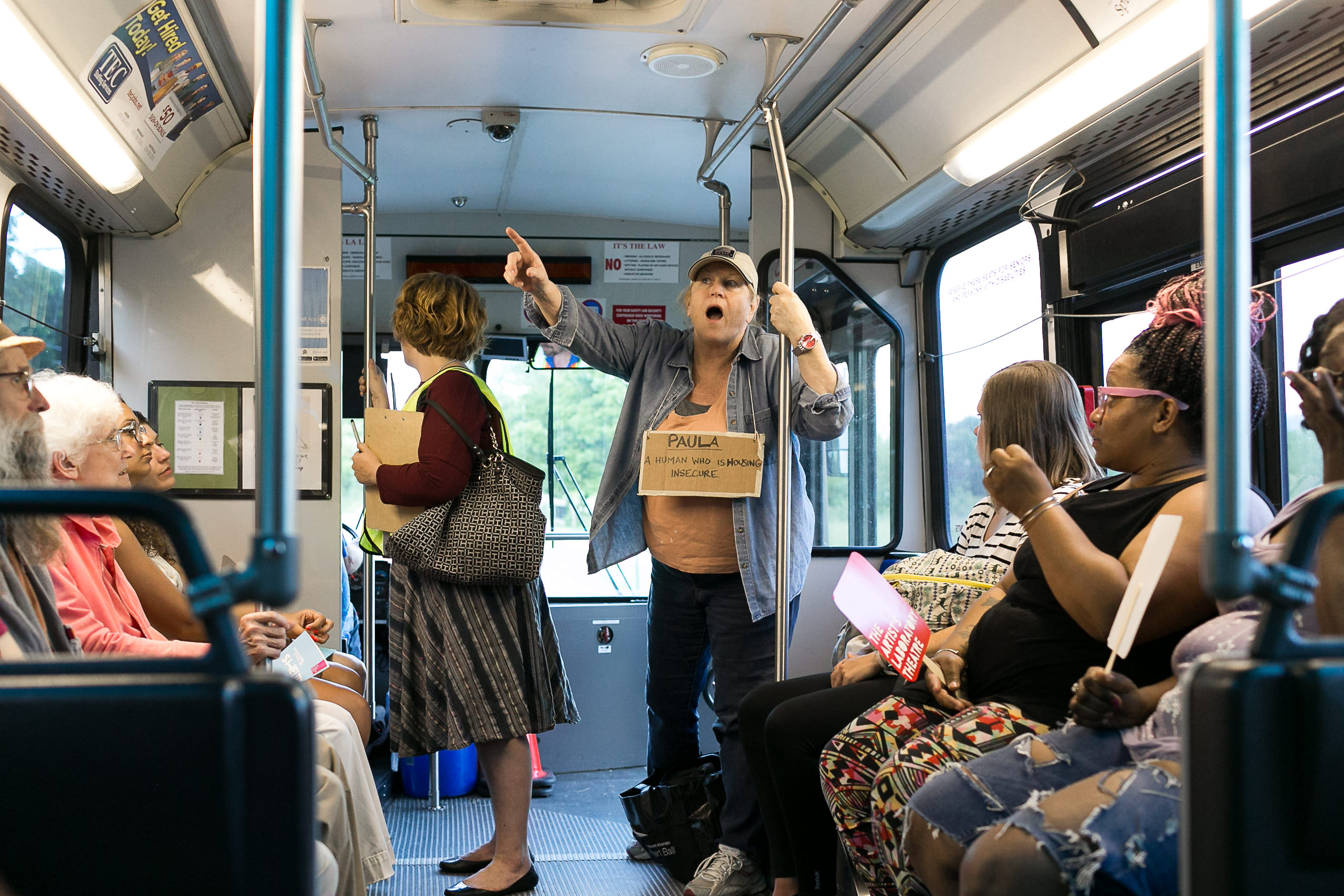 A woman, wearing a sign, stands and points a finger inside a bus.
