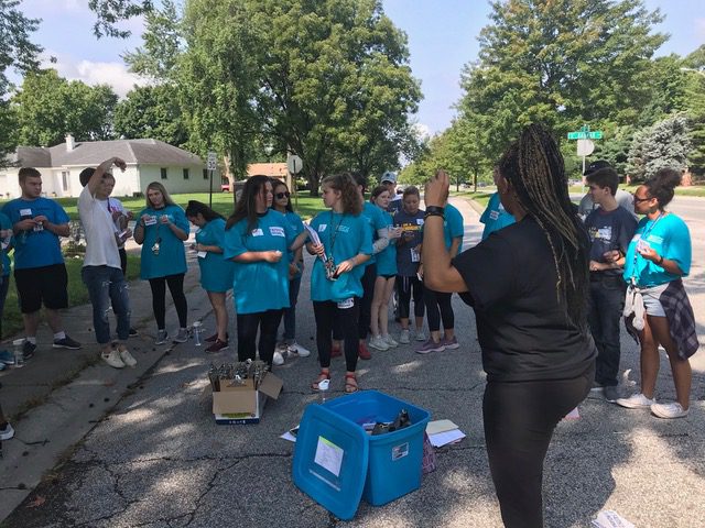 Nicole Barnes, in Black, speaks with a team of canvasses on a street. They are wearing blue.