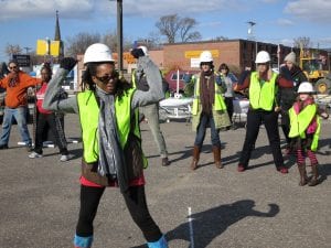 A group of people in yellow vests and hard hats dance.